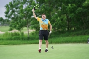 A male golfer waves his hat in the air participating in the STARS of the Spectrum Golf program (Flutie Foundation for Autism).